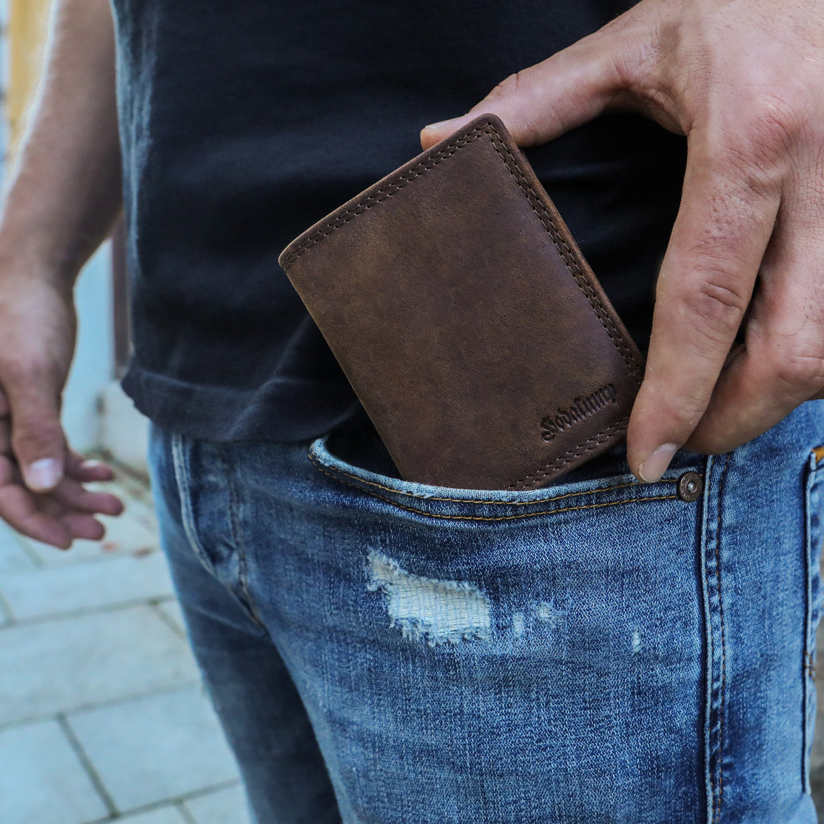 Mann steckt eine schmale braune Lederbörse in die Hosentasche