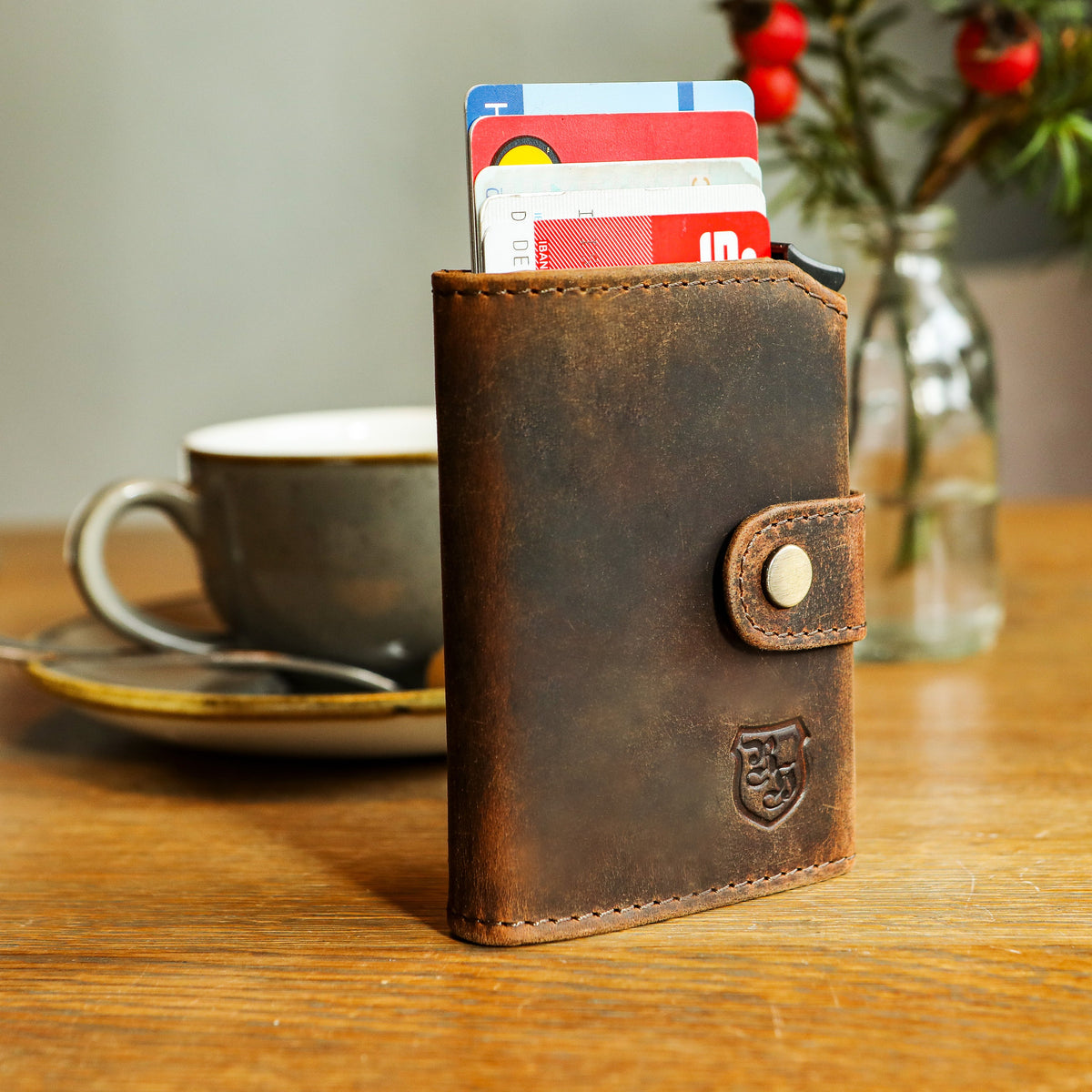 Braunes Kartenetui aus Leder mit herausgeschobenen Karten auf einem Holztisch, daneben eine Kaffeetasse – Wichtelgeschenk unter 50 Euro